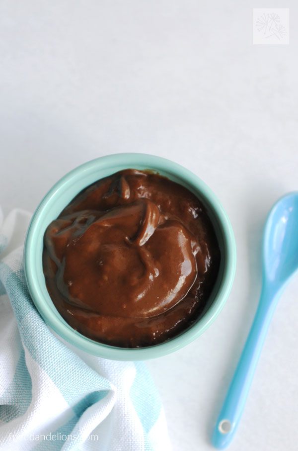 bowl of vegan chocolate pudding with blue spoon and white background
