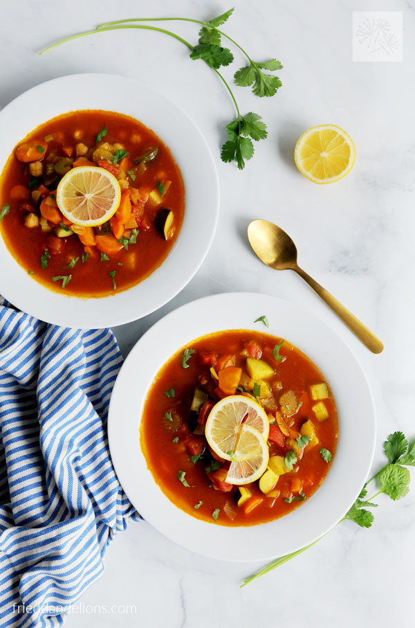 two bowls of Curried Garbanzo Soup with Tomato Broth with gold spoon, sliced lemon, cilantro