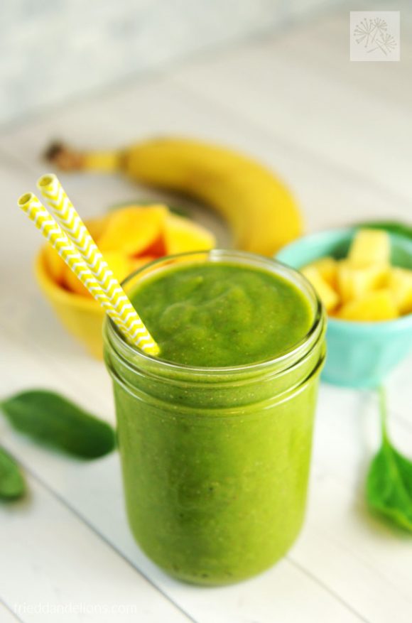 mason jar filled with green smoothie with banana, pineapple, and mango in the background