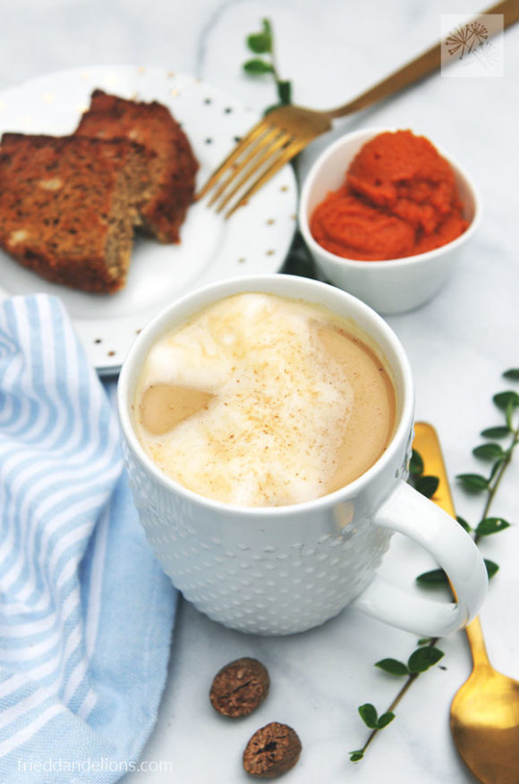 mug of vegan pumpkin spice latte with pumpkin and slice of banana bread in background