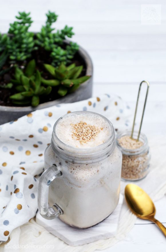 mason jar mug of Tahini Date Shake with pot of succulents in the background and gold spoon in foreground