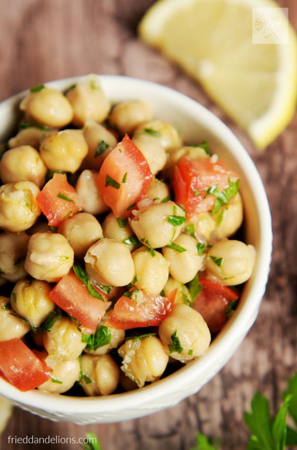 white bowl of chickpea salad on wooden table with lemon wedge