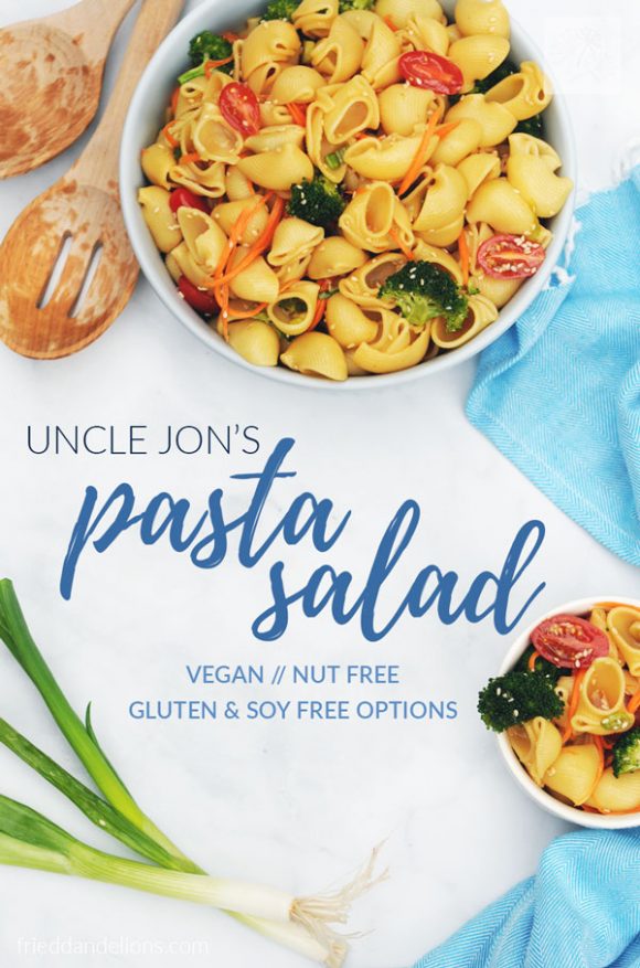 vegan pasta salad in two white bowls with blue napkin, green onions, wooden salad tongs, and white background