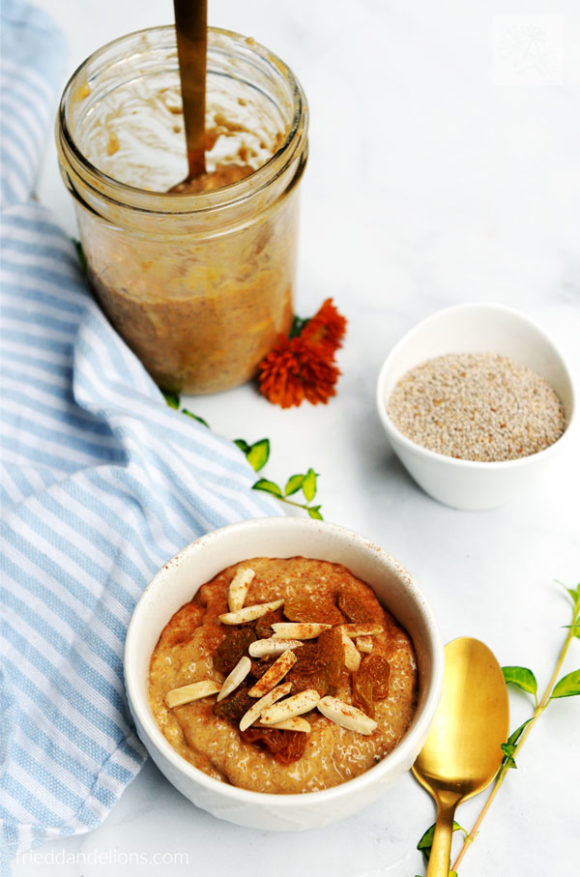 bowl of pumpkin pie chia pudding , with jar of chia pudding in background, bowl of white chia seeds, gold spoon, greens and orange mum, blue striped napkin