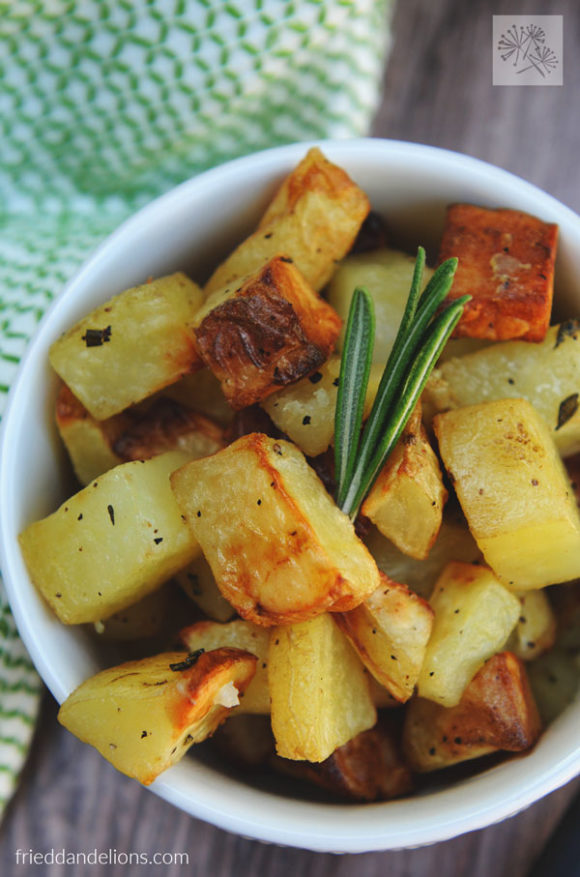 air fryer roasted potatoes in a white bowl with a sprig of rosemary, green napkin, and wood slab background