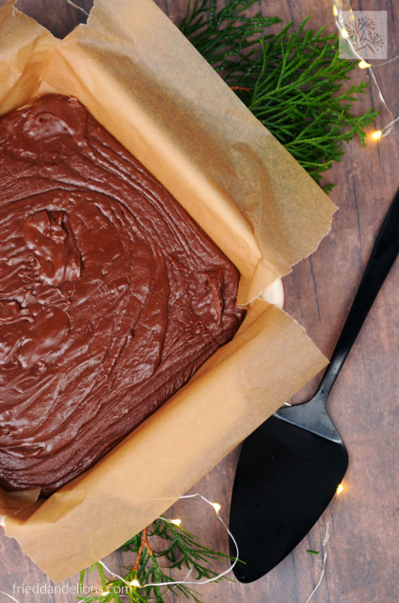 pan of vegan never fail fudge with black pie server, greens, and christmas lights