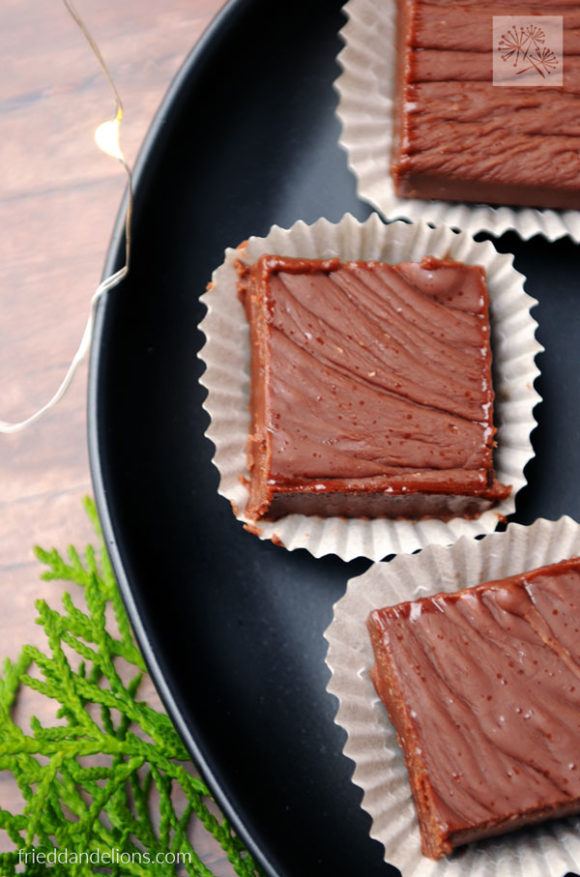 black plate with vegan never fail fudge, greens, Christmas lights in background