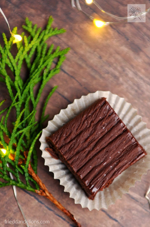 square of vegan never fail fudge with greens, wooden table, Christmas lights in background