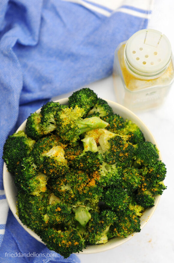 overhead of curry air fried broccoli with blue napkin and jar of curry powder in background