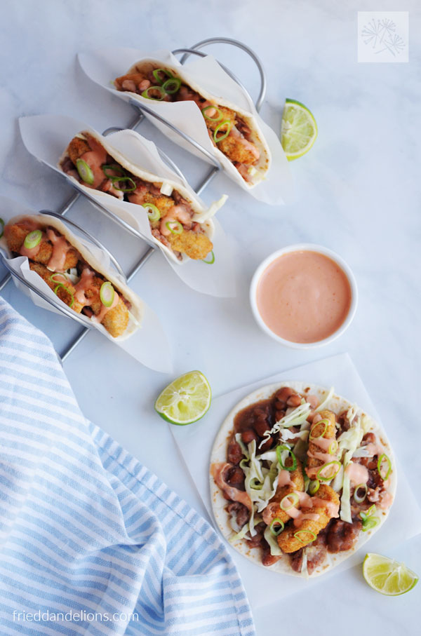 overhead view of Vegan Crispy Chicken Tacos in a taco holder with an open faced taco and a bowl of mayochup in the background, lime wedges, and blue striped napkin