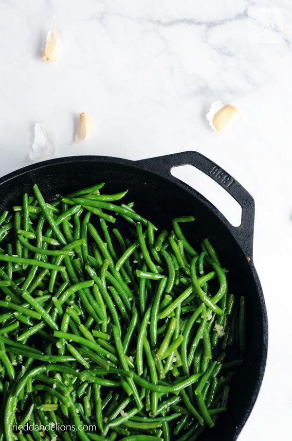 overhead view of green beans with garlic in a cast iron skillet on white marble countertop