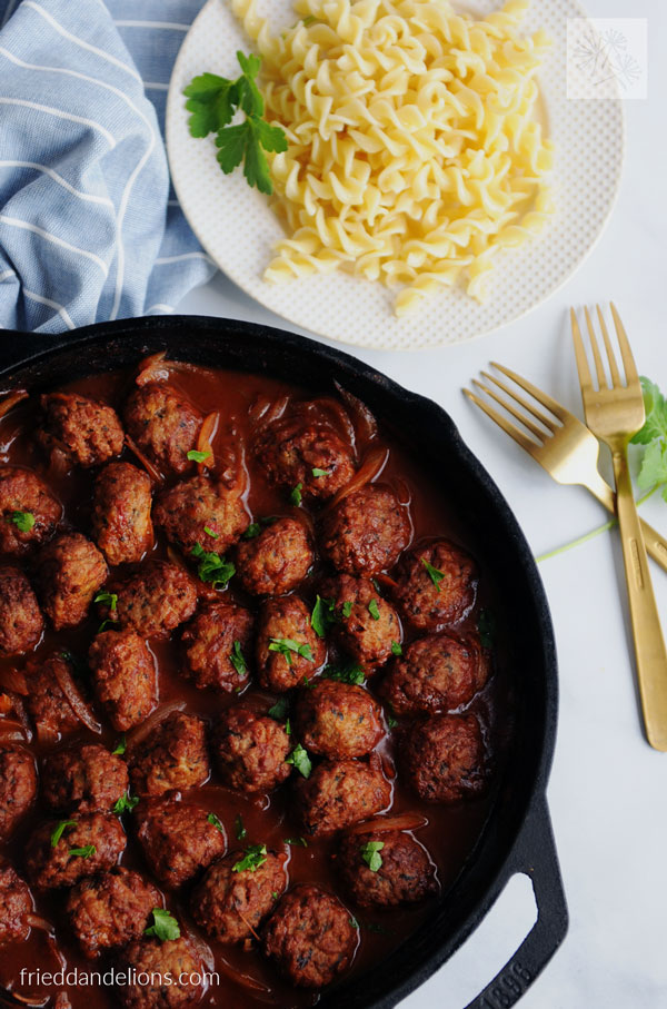 overhead view of skillet of vegan meatball and onion stew with plate of fusilli pasta