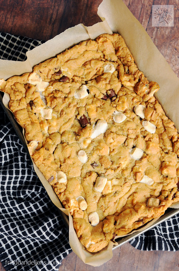 sheet pan of s'mores cookie bars lined with parchment, black and white dishtowel in background