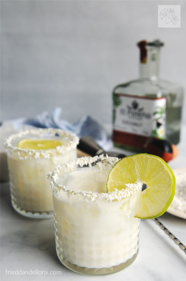 coconut lime margarita garnished with lime slices with coconut tequila in background