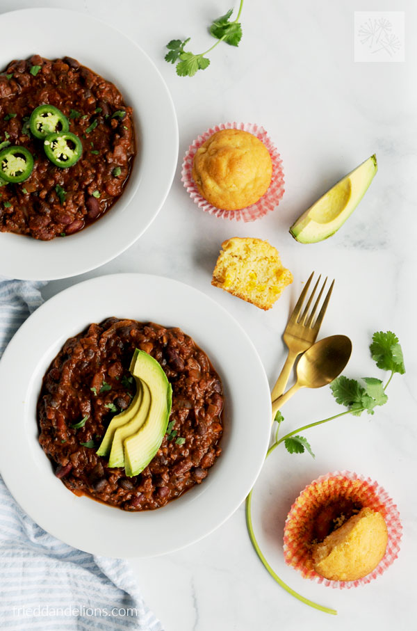 overhead view of two bowls of easy vegan chili, cornbread muffins, avocado slices