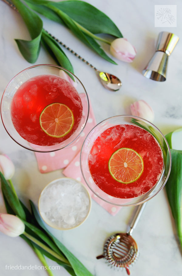 two cosmopolitan cocktails with ice, jigger, tulips in background