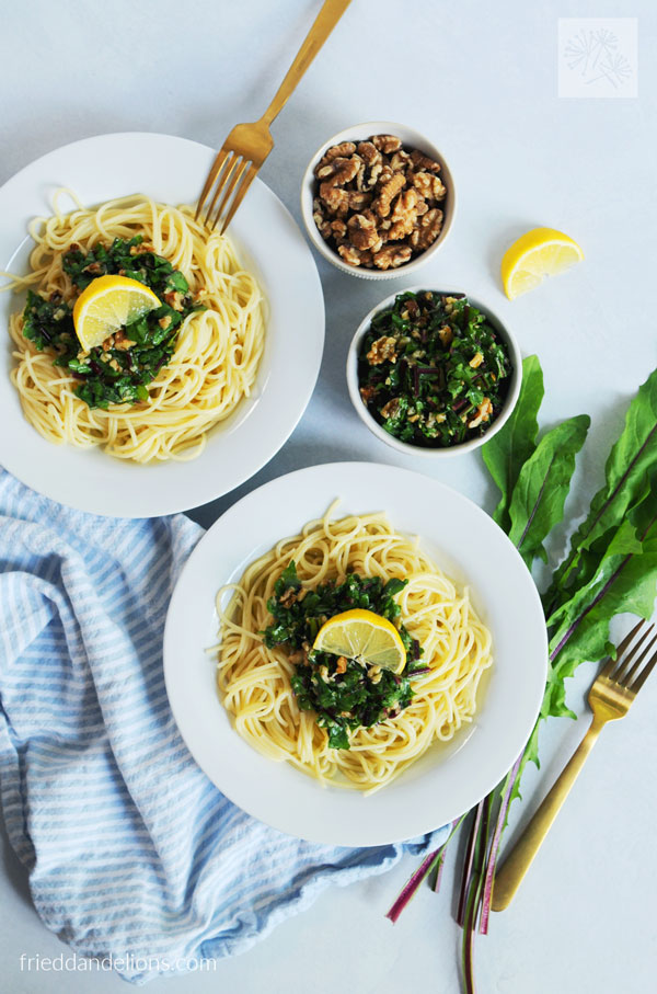 two bowls of pasta topped with Dandelion Greens Gremolata with walnuts, lemon, greens in background
